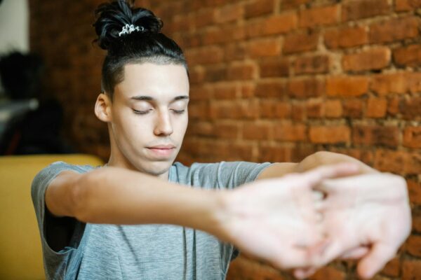 Young male athlete with creative hairstyle cracking knuckles and closing eyes while doing exercise